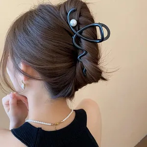 Elegant black French shark hair clip with a pearl accent worn on a stylish bun.