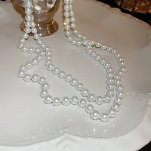 Detailaufnahme einer eleganten langen weißen Perlenkette auf einem dekorativen weißen Teller