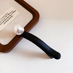 Close-up detail of a matte black hair clip featuring a large lustrous white pearl
