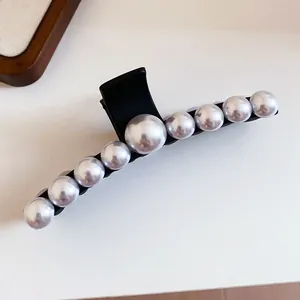 Macro view of elegant black hair claw clip decorated with a row of graduated white pearls