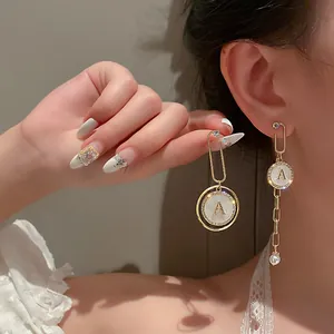 Vue détaillée de boucles d'oreilles asymétriques dorées avec lettre A et une perle.