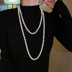 Detailansicht einer langen weißen Perlenkette auf einem schwarzen Rollkragenpullover.