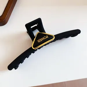 Close-up detail of matte black hair claw clip with gold triangle POWER ornament.