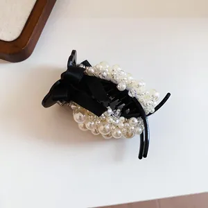 Detailed view of an elegant black hair claw clip with white pearls and a silk ribbon bow