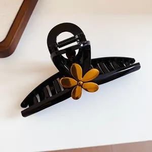 Detail view of a black shark hair claw clip decorated with a golden metallic flower