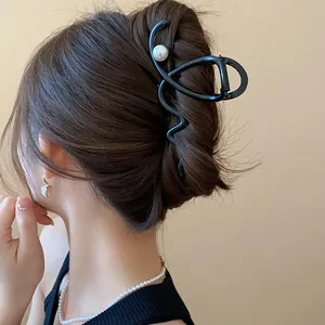 Detail view of an elegant black French shark hair clip with a pearl on dark hair.