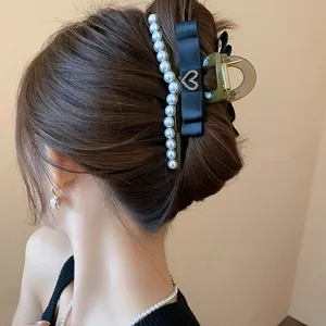 Detail view of an elegant black pearl shark hair clip with heart rhinestone on a hair bun
