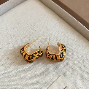 Boucles d'oreilles créoles dorées avec motif léopard sur un plateau de présentation beige