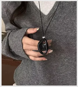 Close-up detail of a minimalist black resin hollow oval pendant necklace on a knit sweater.