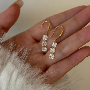 Close-up of elegant gold drop earrings with three round cubic zirconia stones