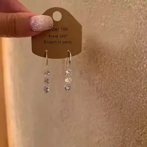 Detail view of silver drop earrings with three clear cubic zirconia stones on display card