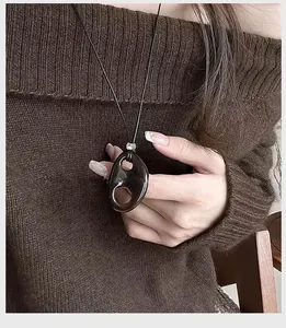 Macro view of a dark resin hollow oval pendant necklace worn on a brown knit sweater