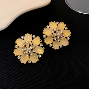 Détail des boucles d'oreilles fleurs dorées avec cristaux étincelants et pétales dépolis.