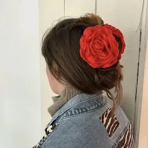 Close-up of a large red fabric rose hair claw clip worn on a woman's brown hair bun