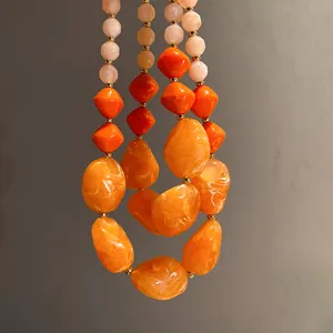 Detailansicht einer klobigen orangefarbenen Acrylperlenkette mit Marmorstruktur.