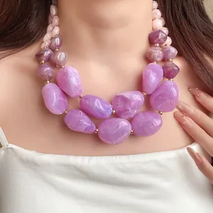 Nahaufnahme einer stylischen mehrlagigen lila und rosa Acrylperlenkette an einem Model.