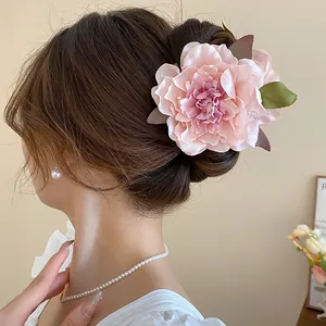 Elegant pink fabric peony flower hair claw clip worn on a stylish low bun hairstyle.