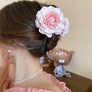 Detail view of a large pink fabric flower hair claw clip on an elegant updo hairstyle.