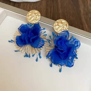 Close-up of vibrant blue fabric flower earrings with textured gold metal studs.