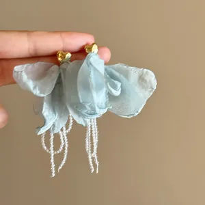 Detail shot of blue fabric flower earrings with golden heart studs and beaded tassels