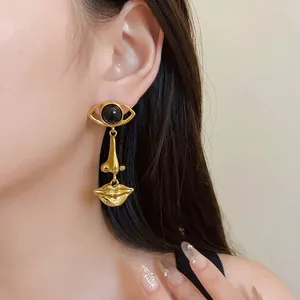 Vintage-style gold asymmetrical earrings with unique eye and lip motifs on a model.