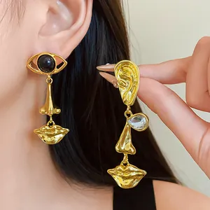 Detailed view of gold asymmetric earrings featuring artistic eye, nose, and lip charms