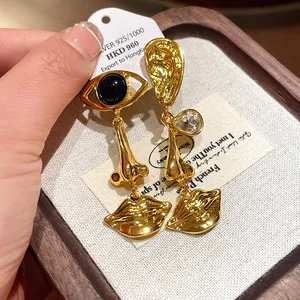 Detailed view of vintage gold-tone asymmetric earrings with surreal face motifs