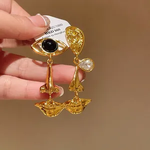 Detail of gold-tone asymmetric earrings featuring artistic eye and mouth motifs