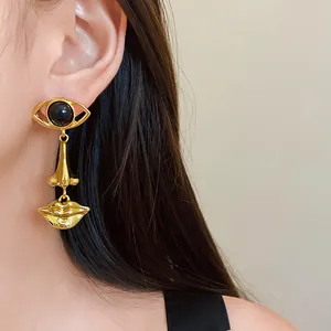 Detailed view of gold surrealist eye nose and mouth dangle earring on model
