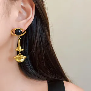 Close-up detail of surrealist eye, nose, and mouth gold drop earrings on an Asian model