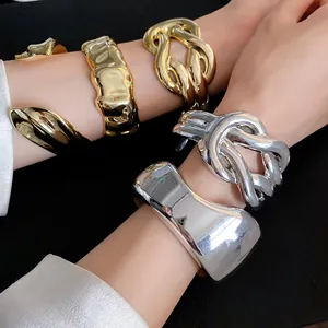 Macro detail of chunky gold and silver glossy geometric open cuff bracelets worn on wrists