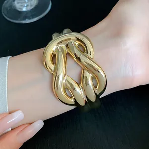 Detailed close-up of a chunky gold knotted acrylic cuff bracelet worn on a wrist