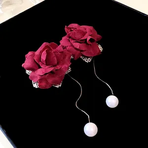 Detailed view of red fabric rose drop earrings with long chains and white faux pearls.