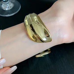 Close-up of a gold glossy pleated geometric open cuff bracelet worn on a wrist