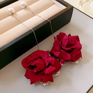Close-up detail of vintage style long earrings featuring red fabric roses and faux pearls.