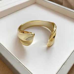 Close-up view of a gold-toned glossy pleated geometric open cuff bracelet in a tray