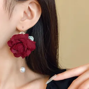 Detail close-up of a burgundy fabric rose earring with an elegant dangling pearl
