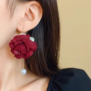 Detail of burgundy fabric flower drop earrings with a white pearl pendant on a long chain