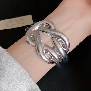 Detailed view of a silver-toned chunky geometric knotted cuff bracelet worn on a wrist