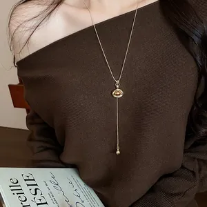 Elegant gold-tone long pendant necklace on a Maillard brown sweater