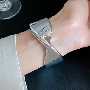 Close-up of a silver shiny wrinkled geometric open cuff bracelet worn on a female wrist