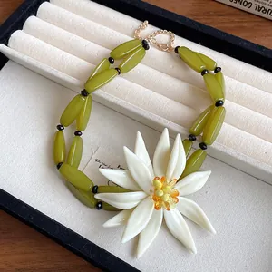 Detailed view of 3D white flower necklace with olive green beads on a jewelry tray