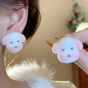 Detailed macro view of cute white fuzzy puppy stud earrings worn on ear and held in hand