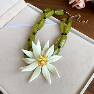 Close-up of olive green beaded necklace featuring a large white 3D floral pendant.