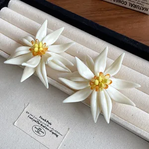 Detailed macro view of white 3D floral earrings with yellow beaded centers on display tray