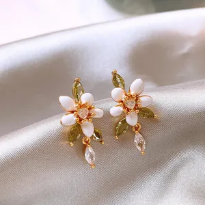 Detailansicht von 14K vergoldeten Blumenohrringen mit weißer Emaille und grünen Zirkonen.
