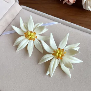 Detail showing elegant white 3D flower earrings with yellow beaded centers and silver needles