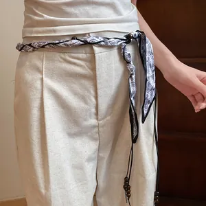 Detail view of bohemian silk scarf woven belt with wooden beads on linen pants.