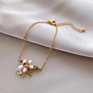 Detailansicht eines goldfarbenen Armbands mit weißer Emaille-Blume und grünen Zirkonia.