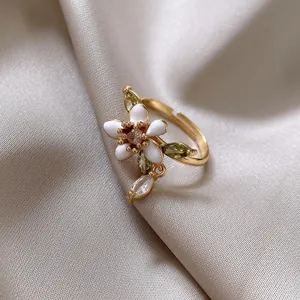 Makroansicht eines vergoldeten Rings mit weißer Emaille-Blume und grünen Zirkonia-Blättern